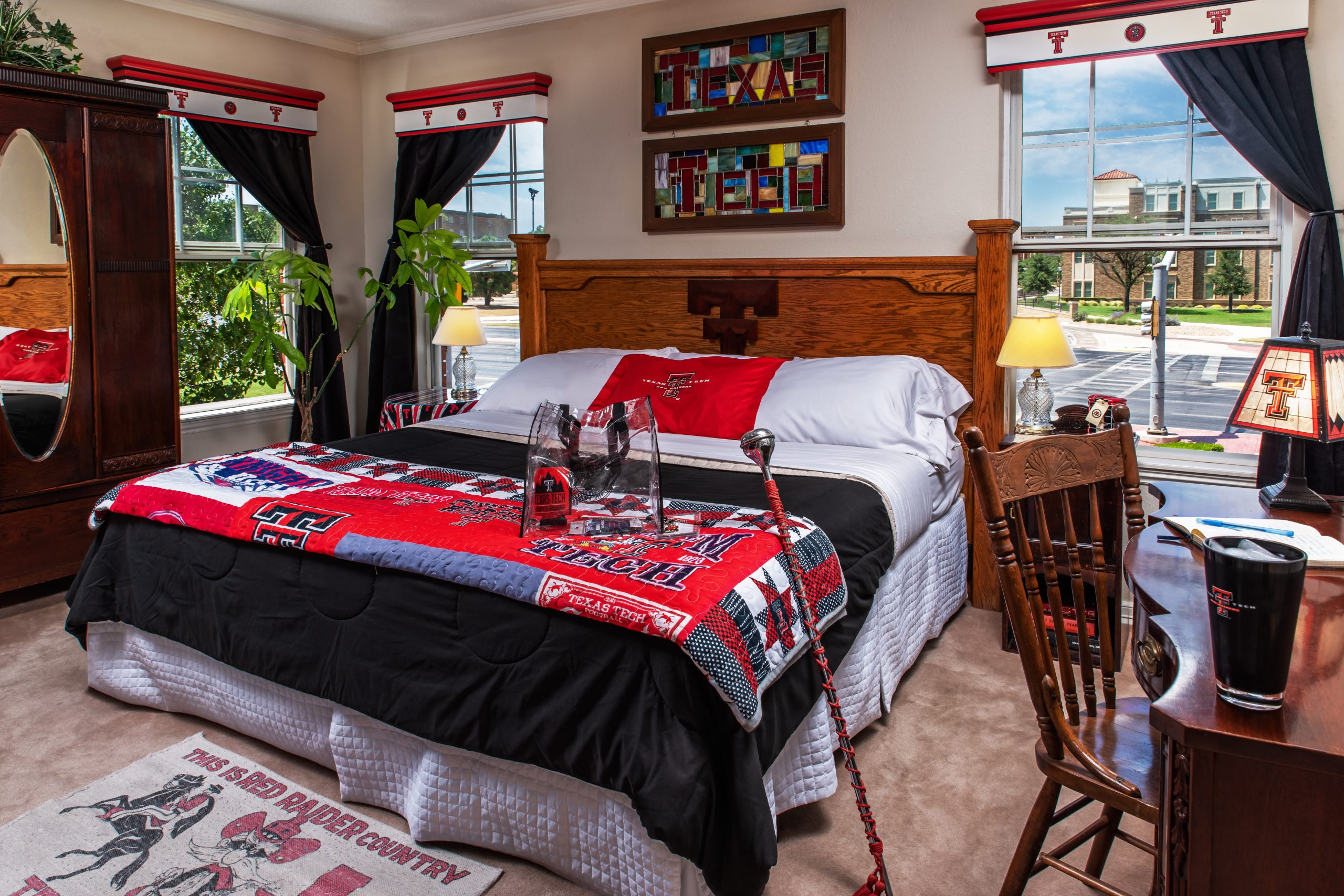 A bedroom at Woodrow House Bed & Breakfast decorated with Texas Tech University items, including a red and black blanket, pillows, and pennants. Sunlight fills the room with a desk and plants—perfect Texas Tech lodging near campus.